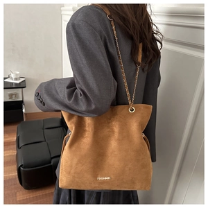 Detalle de bolso tote de ante marrón con cadena dorada y logotipo en color oro