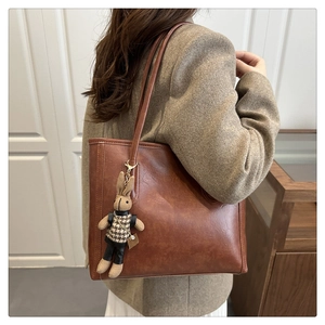 Detail of a brown leather tote bag with a cute rabbit charm on a neutral background