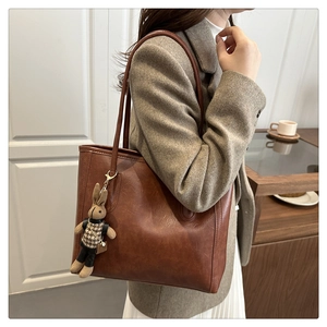 Brown leather tote bag with long straps and a cute plush rabbit charm on a grey blazer model