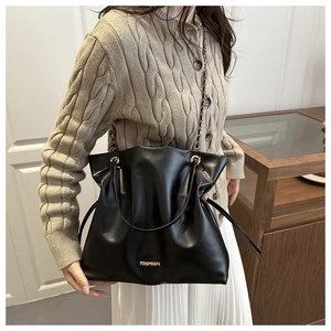 Detail of black faux leather bucket bag with gold FASHION logo and chain strap
