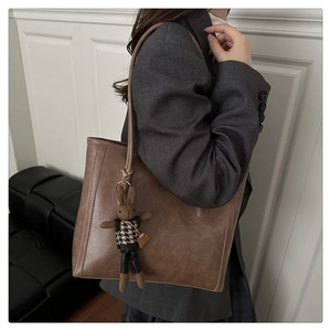 Detail of dark brown leather tote bag featuring a decorative bunny charm and long shoulder strap