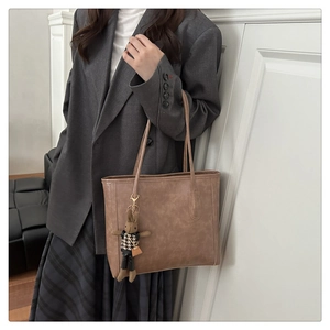 Classic tan leather tote bag with a cute rabbit charm shown on a stylish model