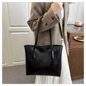 Detail of a large black faux leather tote bag on a wooden table with coffee and croissant
