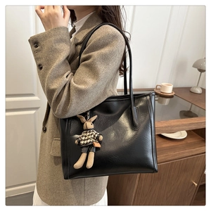 Detail of black leather tote bag featuring a lychee texture and cute rabbit charm pendant