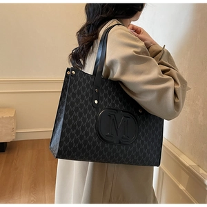 Detail of black tote bag with letter M jacquard pattern worn over the shoulder