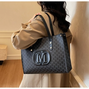 Detailed view of large tote bag with M-pattern and gold rivet accents on shoulder strap