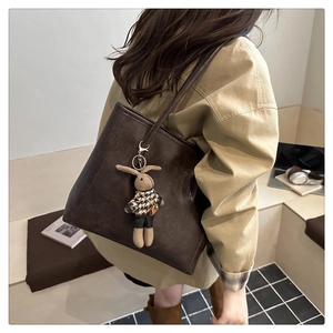 Detail view of large dark brown leather tote bag with a houndstooth rabbit pendant