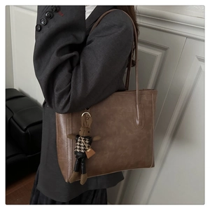 Detail view of large brown tote bag with vintage rabbit charm and matte leather texture