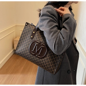 Makroansicht der braunen Retro-Tote-Bag mit M-Buchstaben-Monogramm und Leder-Tragegriffen