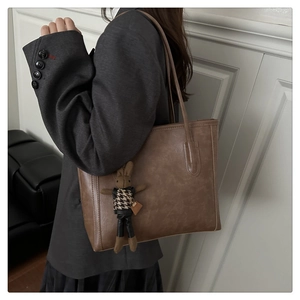 Detail of coffee brown leather tote bag with a cute rabbit charm and shoulder strap