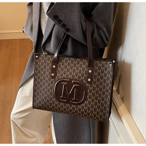 Detailansicht einer großen Shopper-Tasche mit braunem M-Muster und Lederhenkeln