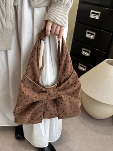 Brown corduroy tote bag with large bow and black heart floral pattern held by a model