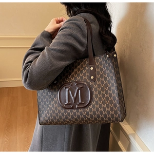 Detailansicht der braunen Monogramm-Einkaufstasche mit M-Logo und Lederriemen