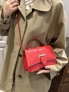 Fashionable red quilted handbag with gold clasp and top handle on trench coat model