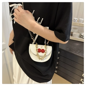 Close-up of white saddle mini bag featuring red cherry decor and chunky gold chain