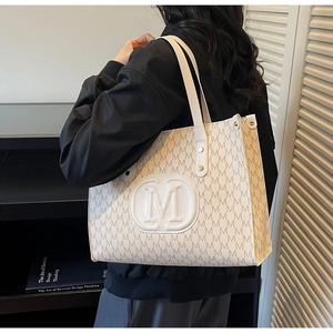 Detail of elegant beige tote bag with M-pattern print and embossed central logo