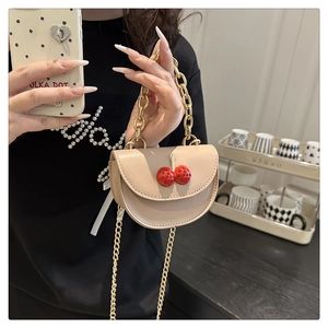 Detail of a beige half-round mini bag with cherry charms and gold chain straps