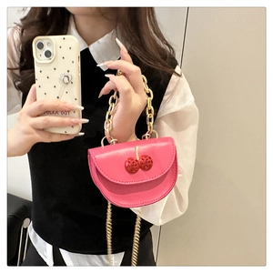 Detail of pink saddle bag featuring 3D cherry decor and golden chain strap