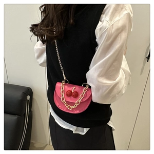 Pink mini saddle bag featuring cherry pendants and gold chain strap worn by a model