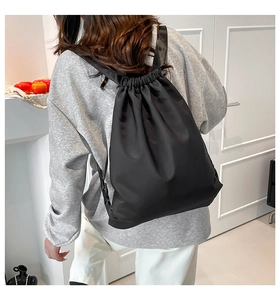 Minimalist black nylon drawstring backpack shown from a side view on a model in a room