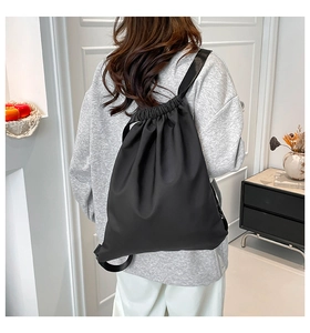 Detail of lightweight black nylon drawstring backpack with wide straps on a model back