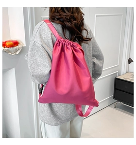 Rear view of model wearing a magenta drawstring backpack with shiny waterproof nylon