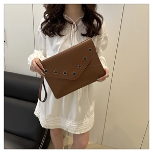 Detail of dark brown leather envelope clutch bag with silver metal eyelet studs and wristlet