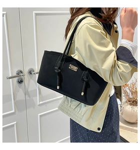 Detail of black quilted tote bag featuring gold logo and sleek shoulder strap styling