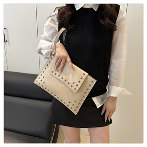 Detail shot of beige envelope handbag with silver square studs held by a model