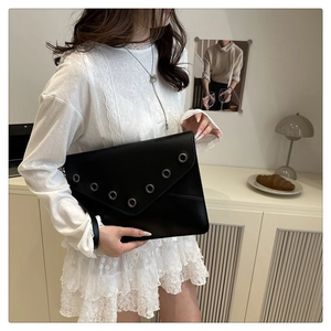 Detail of black envelope clutch featuring silver metal eyelets and a wristlet strap