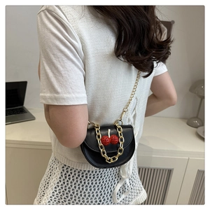 Woman wearing a mini black leather crossbody bag with cherry detail and gold chain strap