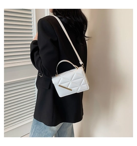 Detail of white quilted crossbody bag with gold metal trim on model with black blazer