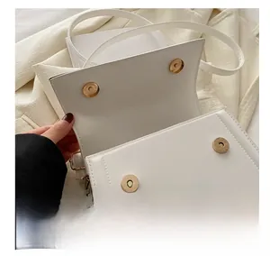Detail view of white minimalist square bag showing golden magnetic closures and smooth leather