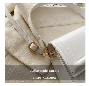 Detailed close-up of adjustable gold buckle and hook on white leather shoulder bag strap