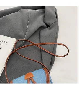Close-up of slender brown leather strap and blue denim texture on the crossbody bag