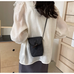 Back view of a grey crossbody bag with horn buckle detail worn by a model in soft light