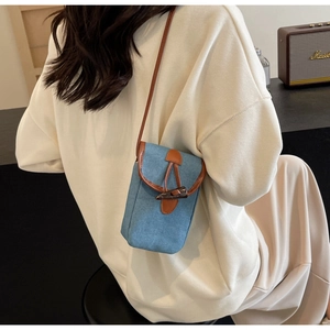 Dettaglio della borsa porta cellulare in denim blu con finiture in pelle e fibbia in corno