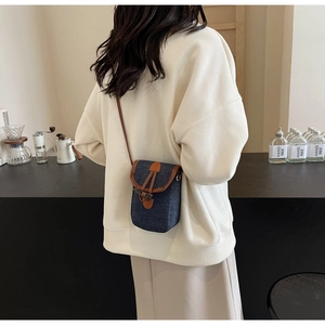 Dettaglio borsa porta cellulare in denim blu scuro con finiture in pelle marrone e fibbia