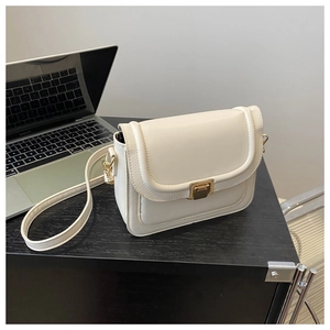 Vue détaillée du sac bandoulière crème avec fermoir doré posé sur un bureau noir