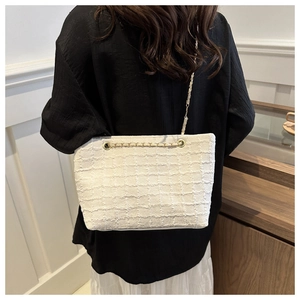 Detail of white tweed crossbody bag with gold chain strap worn on dark casual attire
