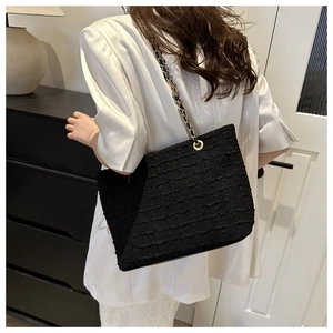 Detail of black textured tweed tote bag featuring gold chain strap on a model shoulder