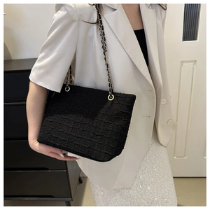 Detail shot of black tweed shoulder bag with gold chain strap worn by a female model