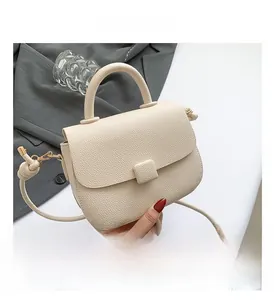 Detail shot of a cream-colored leather handbag showing textured litchi grain and square buckle