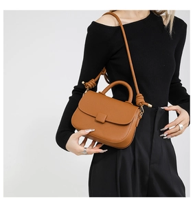 Close-up of brown lychee grain leather saddle bag featuring a decorative knotted shoulder strap