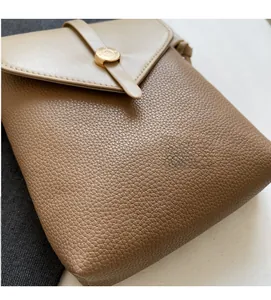 Close-up of brown litchi grain leather texture and gold buckle on a crossbody bag