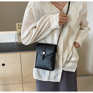Detail of minimalist black pebbled leather crossbody bag with round gold metal buckle