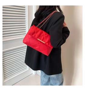 Detail of red quilted crossbody bag with gold buckle and chain strap on female model