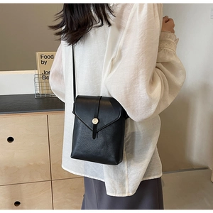 Detail of lychee textured leather crossbody bag with a round gold metallic snap button