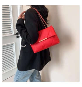 Detail of red quilted shoulder bag featuring gold chain strap and metal lock closure