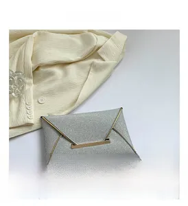 Detailweergave van de zilveren glittertextuur en gouden metalen frame op deze enveloptas